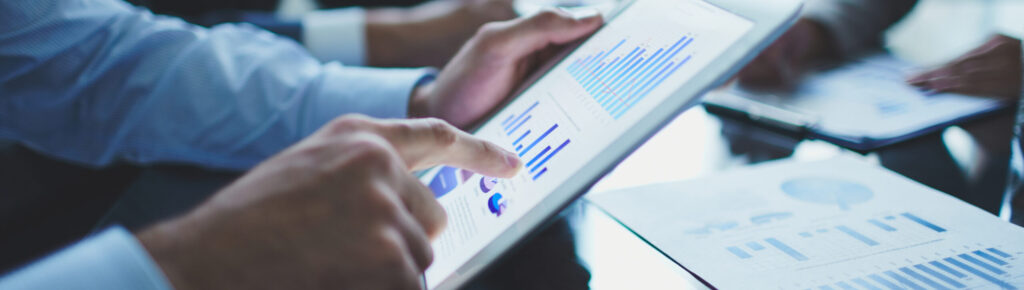 Profissionais analisando gráficos financeiros em tablet digital e relatórios impressos durante reunião corporativa, simbolizando análise de desempenho, estratégias de negócios e tomada de decisão baseada em dados.
