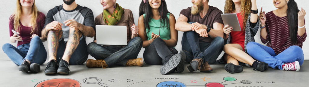 Grupo diverso de jovens sentados no chão interagindo com laptops e tablets, sorrindo e trocando ideias. No chão, há desenhos coloridos que representam conceitos como criatividade, design, pesquisa e inovação.