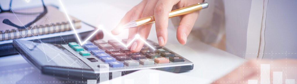 Pessoa usando calculadora com caneta na mão, ao lado de caderno e gráficos, representando análise financeira, planejamento contábil e controle de lucros.