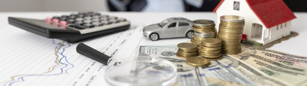 Conceito de planejamento financeiro com pilhas de moedas, notas de dólar, miniatura de casa e carro, calculadora e gráfico de investimentos sobre mesa de escritório.