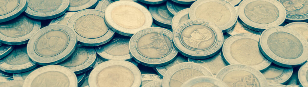 Grande quantidade de moedas tailandesas de 10 baht espalhadas, exibindo rostos e templos tradicionais em suas faces.