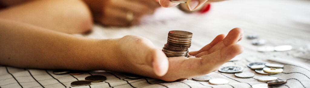 Criança aprendendo sobre educação financeira com adulto, empilhando moedas sobre a mão, representando o ensino do valor do dinheiro e poupança desde cedo.