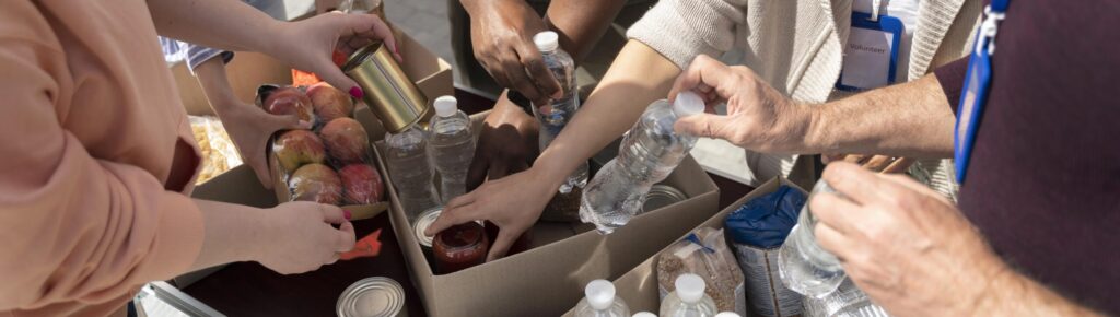 Grupo diverso de voluntários unindo as mãos com sorriso, em ação colaborativa em banco de alimentos, representando solidariedade, trabalho em equipe e engajamento social.