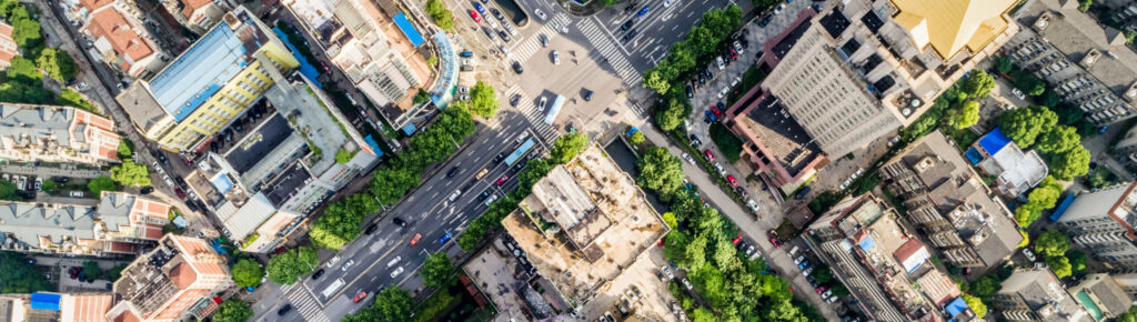 Vista aérea de cruzamento urbano com prédios, ruas movimentadas e áreas verdes, mostrando o planejamento e a infraestrutura da cidade.