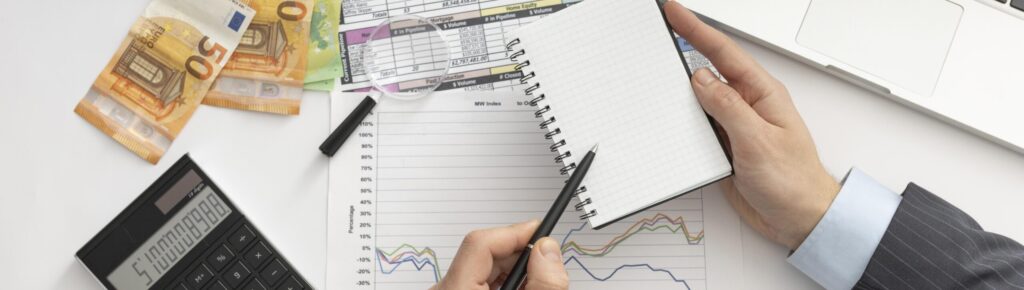 Vista superior de empresário analisando finanças com gráficos, calculadora, notas de euro e laptop, representando planejamento financeiro e gestão de investimentos.