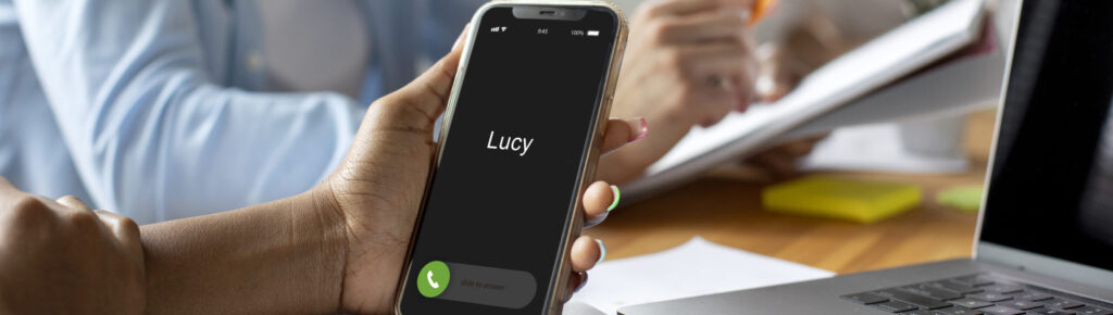 Mulher recebendo uma ligação de negócios em seu smartphone durante reunião de trabalho, com colegas discutindo anotações e laptop sobre a mesa, simbolizando comunicação, networking e produtividade.