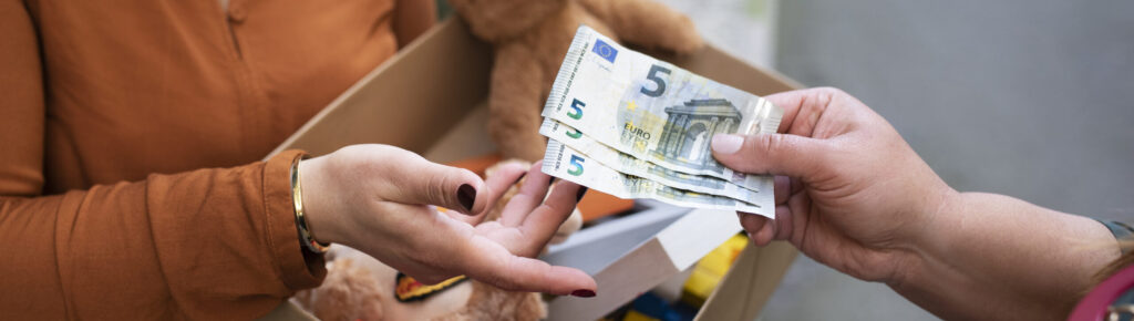 Mulher entregando dinheiro em troca de caixa com brinquedos usados, simbolizando consumo consciente, economia solidária, reaproveitamento e apoio a pequenos negócios locais