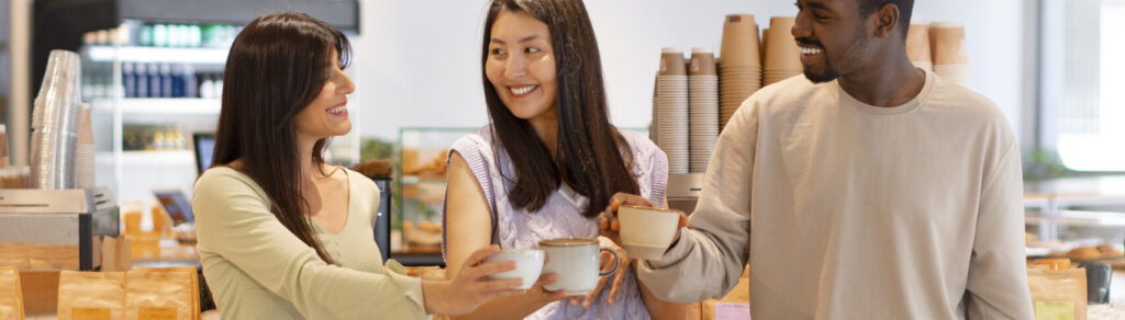 Três amigos sorridentes tomando café juntos em cafeteria moderna e espaçosa