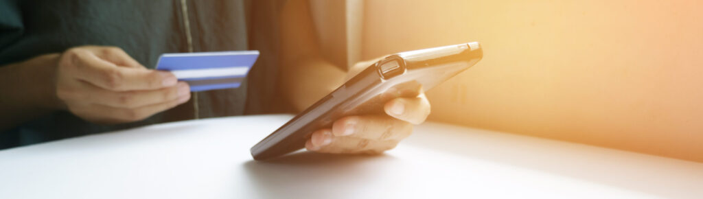 Pessoa segurando cartão de crédito e smartphone para realizar compras online com segurança.