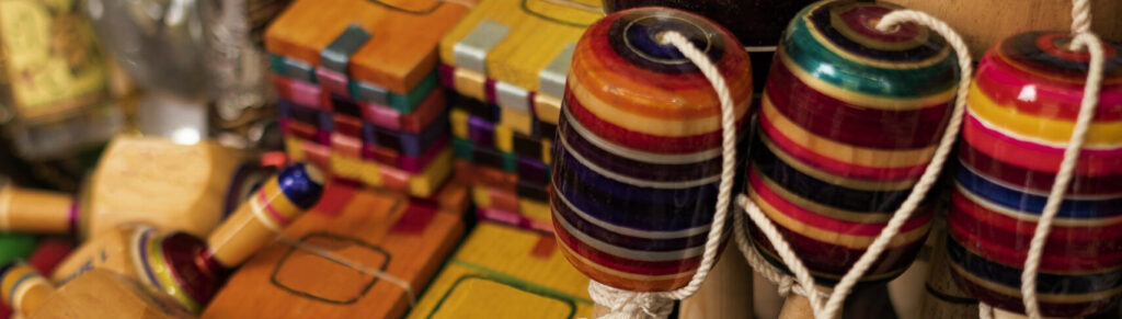 Brinquedos artesanais coloridos de madeira, como piões, matracas e maracas, expostos em feira cultural, representando tradição popular, economia criativa e artesanato sustentável brasileiro.