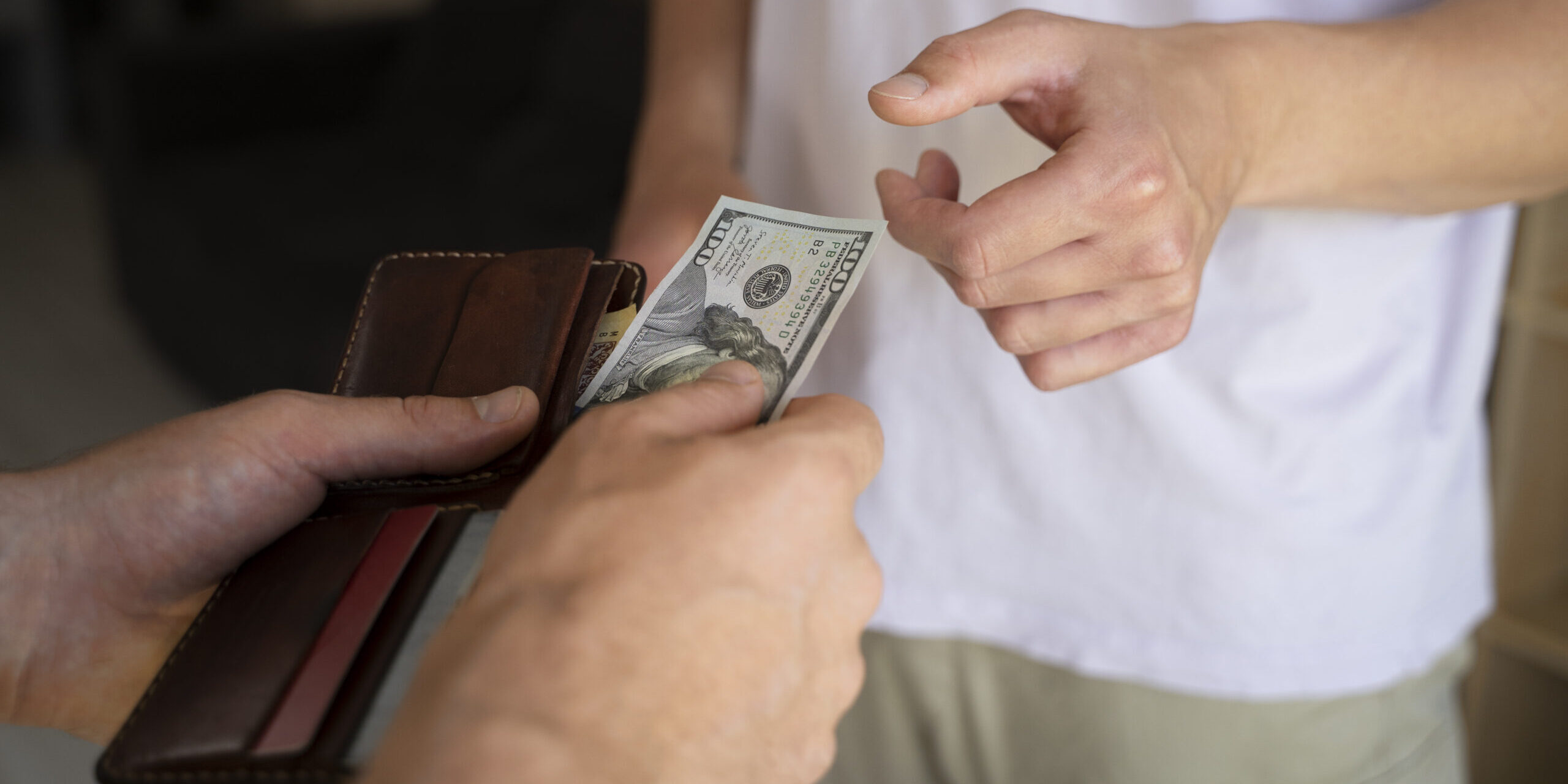 Pessoa entregando nota de dólar em pagamento direto a outra pessoa, simbolizando transação financeira, economia informal, consumo consciente e uso de dinheiro em espécie.